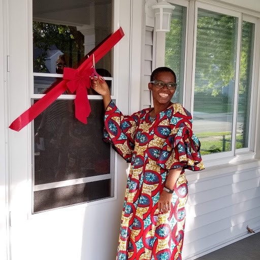 smiling Habitat homeowner dressed in traditional African wardrobe while preparing to cut the red ribbon across her door for her home dedication